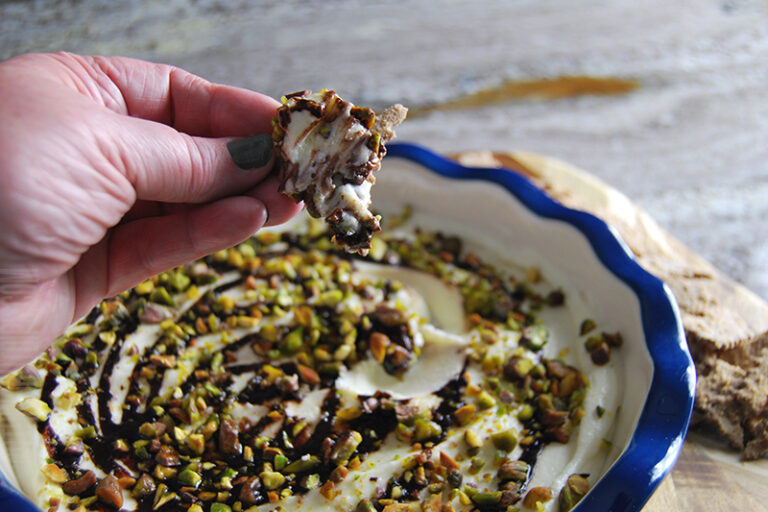 Cannoli dip topped with chocolate syrup and pistachios and served with a cannoli chip