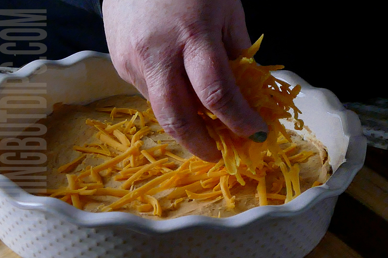 garnishing layered taco dip with shredded cheddar cheese