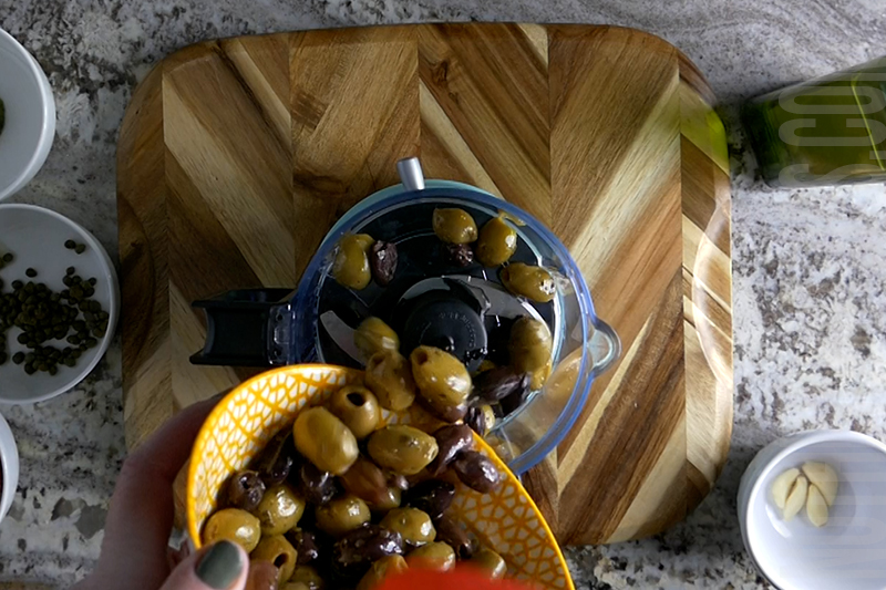 pouring kalamata and green olives into the food processor