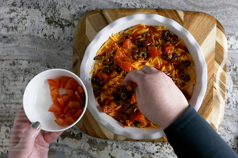 garnishing the layered taco dip with diced tomatoes