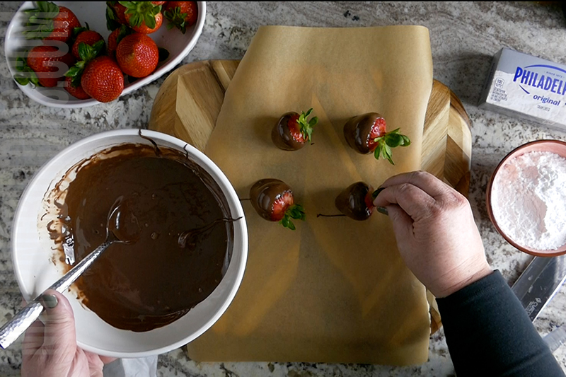 dipping strawberries into melted chocolate to make chocolate covered strawberries