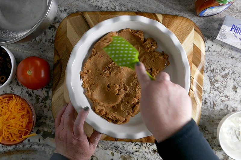 spreading refried beans into the base of the layered taco dip