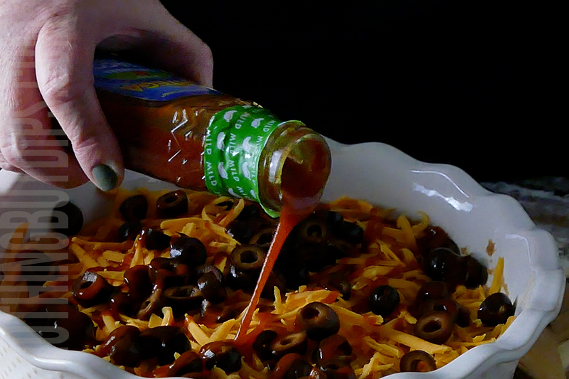 drizzling taco sauce onto the layered taco dip