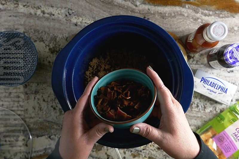 crumbled bacon being added to sweet and sour beef and cheese dip (aka put a ring on it cheese dip)