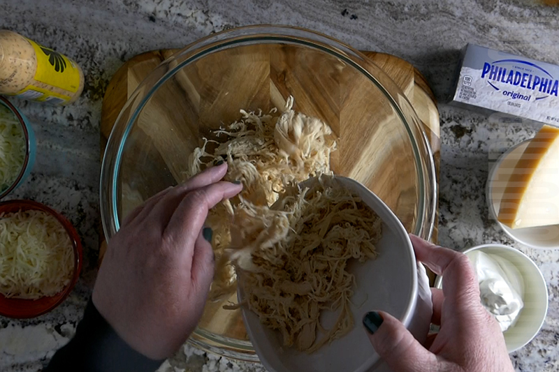 adding shredded chicken to the mixing bowl