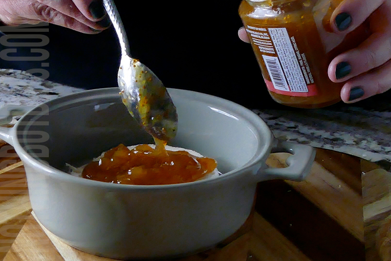 adding fig jam to the top of the brie cheese wheel