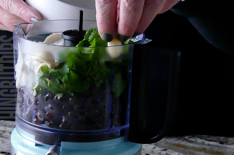 adding garlic to the black bean puree mixture in the mini food processor