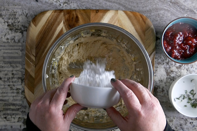 adding powdered sugar to a mixing bowl to make the creamy base for strawberry basil cheesecake dip