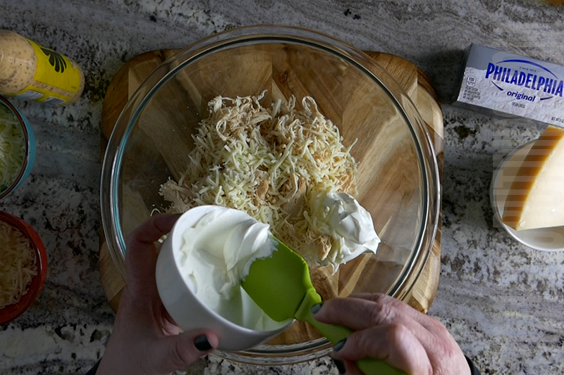 adding sour cream to the mixing bowl to make parmesan garlic wing dip