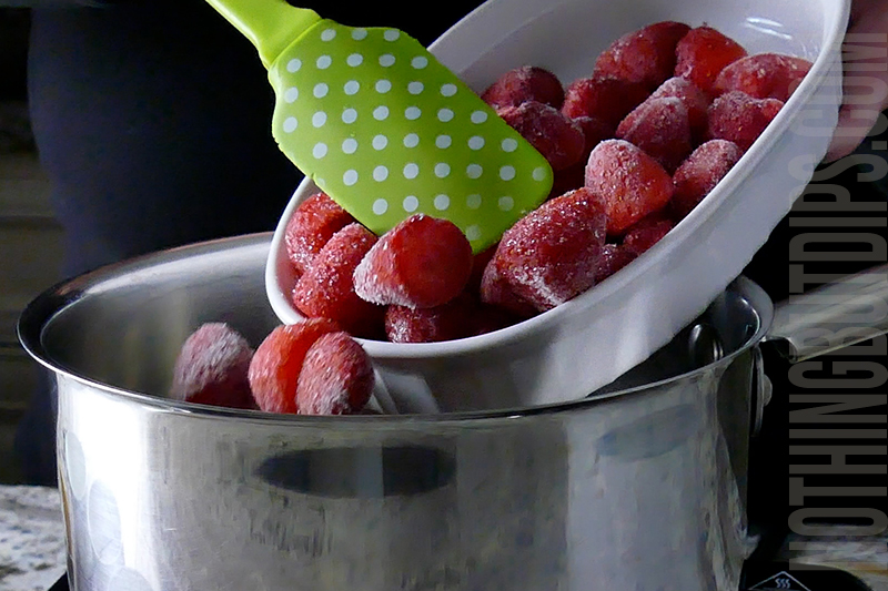 adding the frozen strawberries to a pot to make a compote for the top of the strawberry basil cheesecake dip