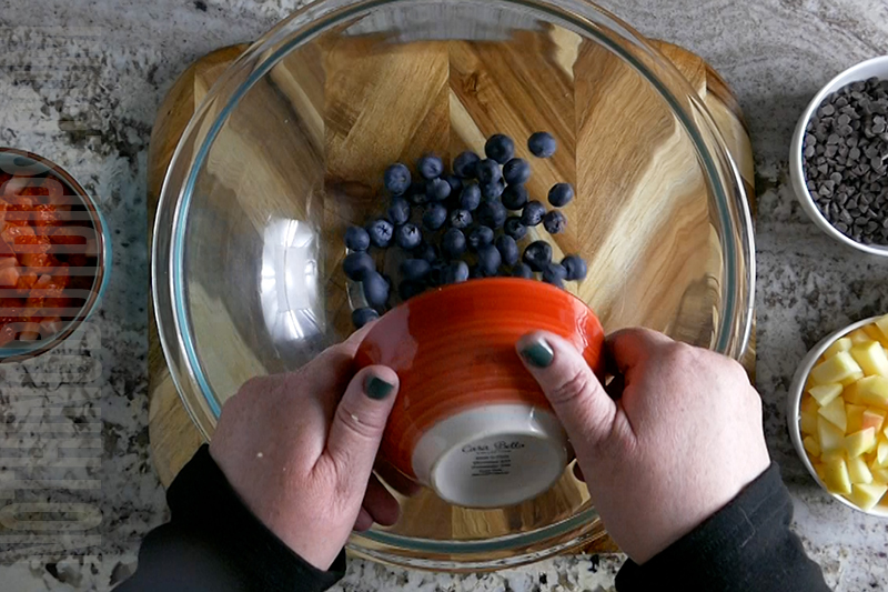 adding blueberries to a bowl to make fruit salsa