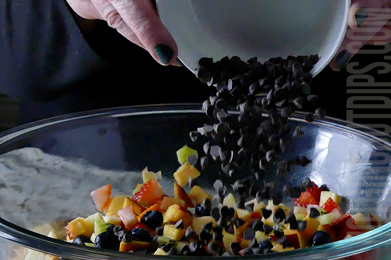 adding mini chocolate chips to a bowl to make fruit salsa