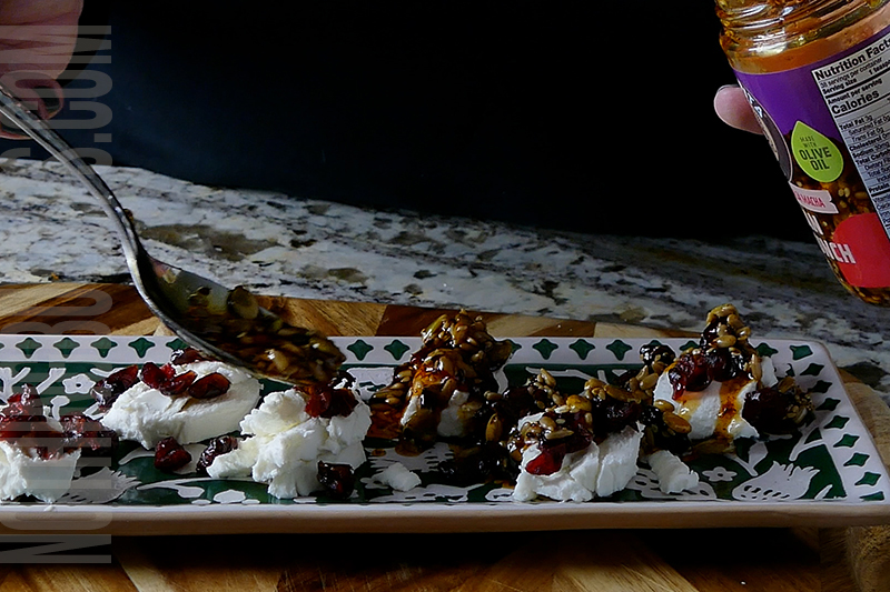 spooning on crunchy chili oil onto the goat cheese pieces and dried cranberries to create marinated goat cheese
