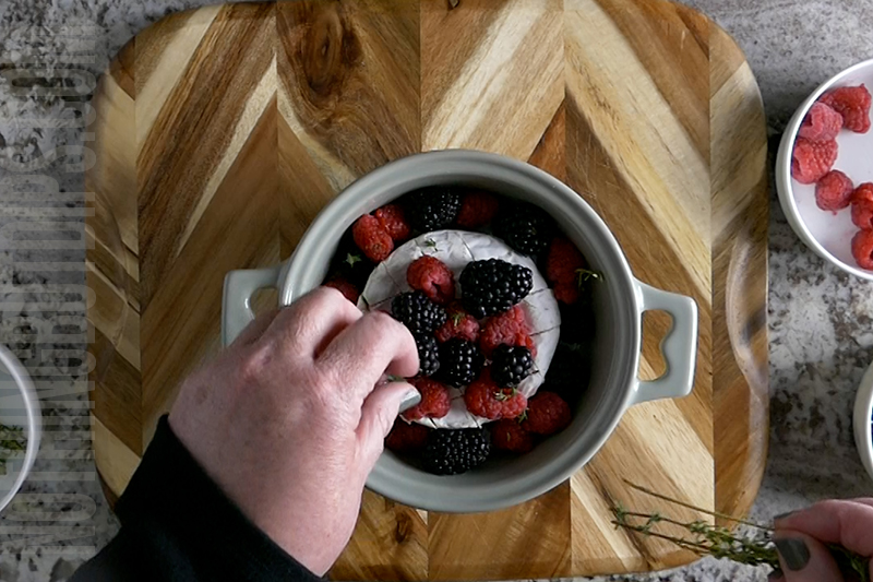adding fresh thyme to the berries on the wheel of brie 