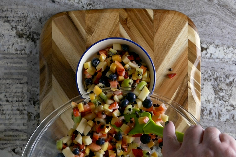 transferring fruit salsa from a bowl to a serving dish