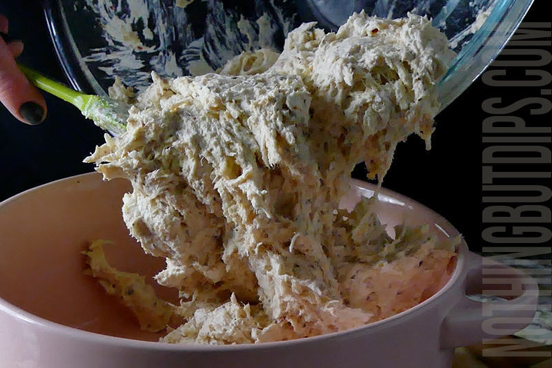 transferring the ingredients to make parmesan garlic wing dip from the bowl to the baking dish