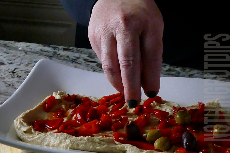layering roasted peppers ad olives on hummus