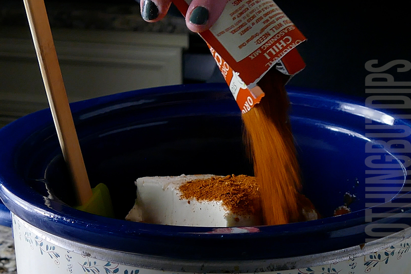 adding chili seasoning to the crockpot to make chili cheese dip