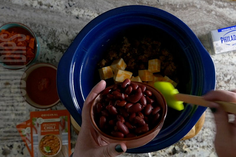 adding drained kidney beans to the crockpot to make chili cheese dip