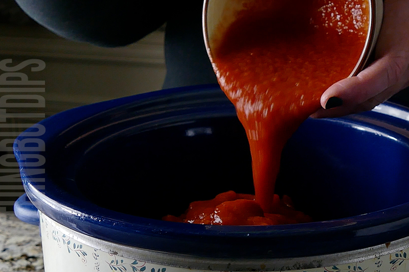 adding tomato sauce to the crockpot to make chili cheese dip