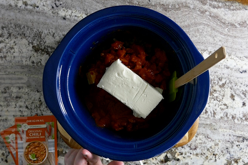 adding creamed cheese to the crockpot to make chili cheese dip