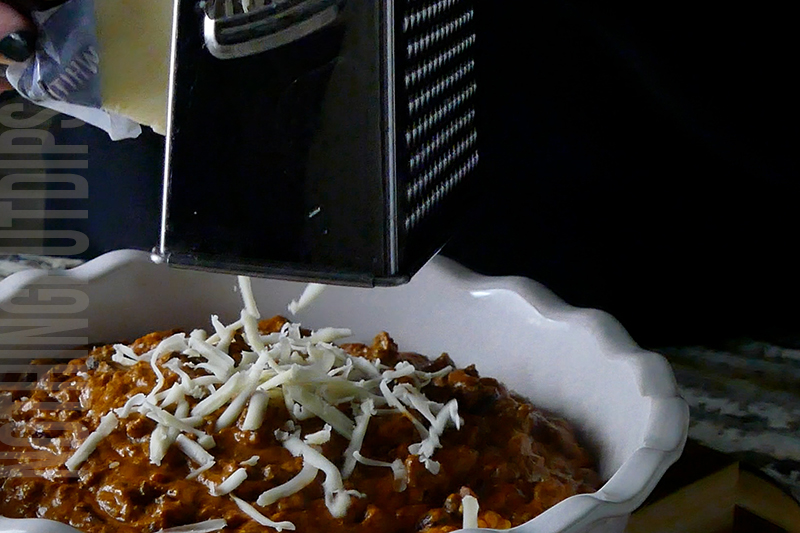 adding grated cheese to the top of the chili cheese dip for serving