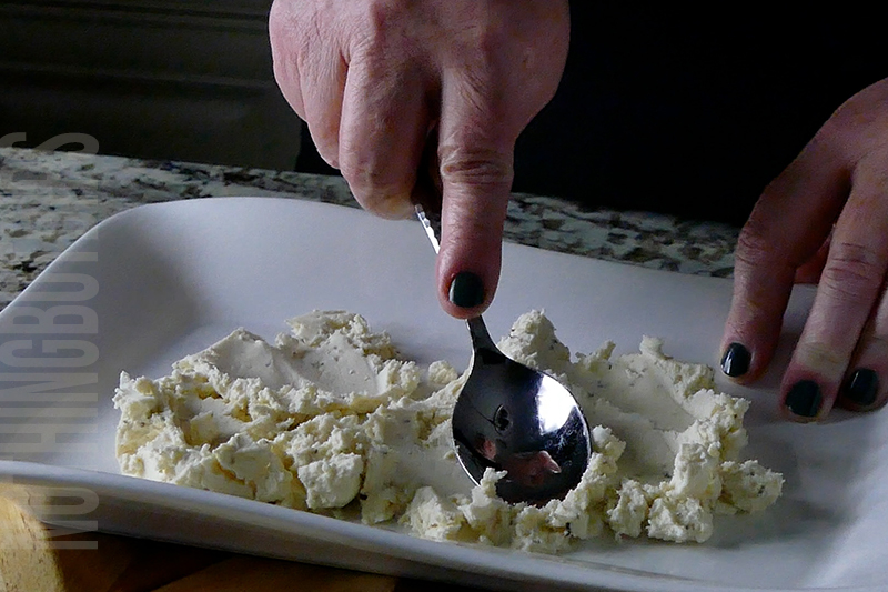 spreading Boursin cheese with a spoon onto a serving platter