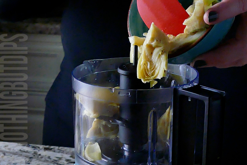 adding jarred artichokes to a mini food processor to make baked artichoke dip