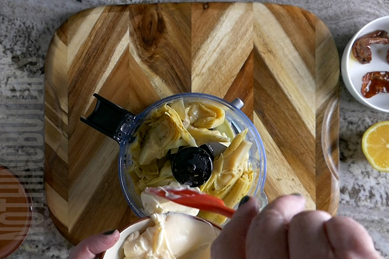 adding mayo to a mini food processor to make baked artichoke dip