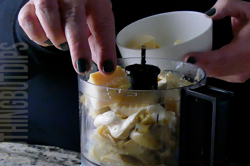 adding parmesan cheese to a mini food processor to make baked artichoke dip