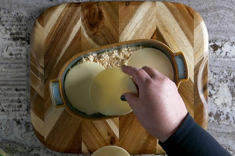 adding slices of provolone cheese to top of artichoke mixture prior to baking to make baked artichoke dip with melted cheese