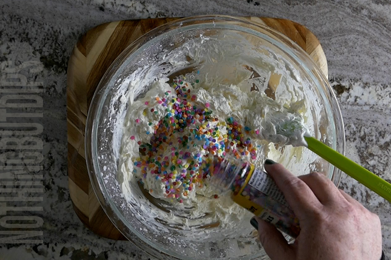 adding sprinkles to the mixture in the bowl to create birthday cake dip