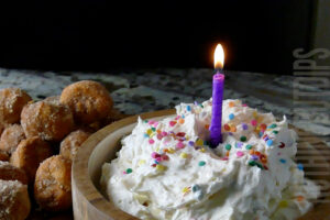 Easy sweet and creamy birthday cake dip with a birthday candle on top and donut holes on the side for serving