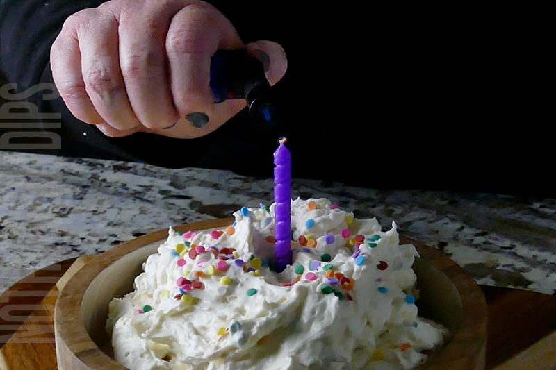lighting a purple birthday candle placed on the top of the birthday cake dip