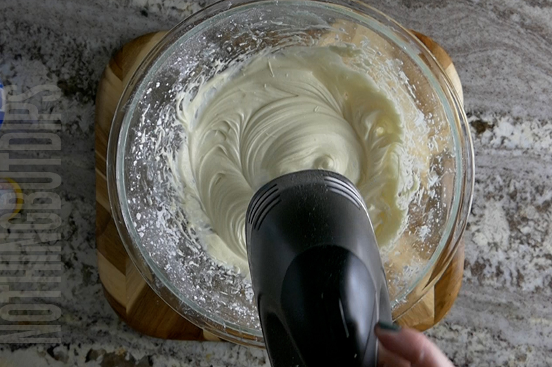 mixing the ingredients with a hand mixer in a glass bowl to make the base of the birthday cake dip
