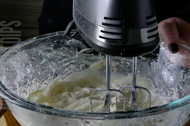 mixing the ingredients with a hand mixer in a glass bowl to make the base of the birthday cake dip