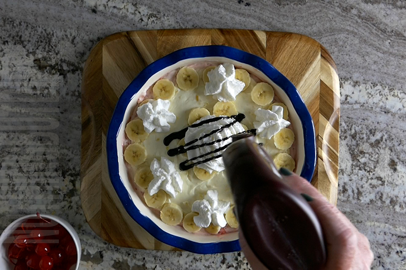 placing whipped cream and chocolate sauce on top of the banana split dip