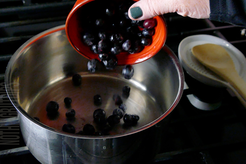 adding frozen blueberries to a sauce pan to make blueberry compote