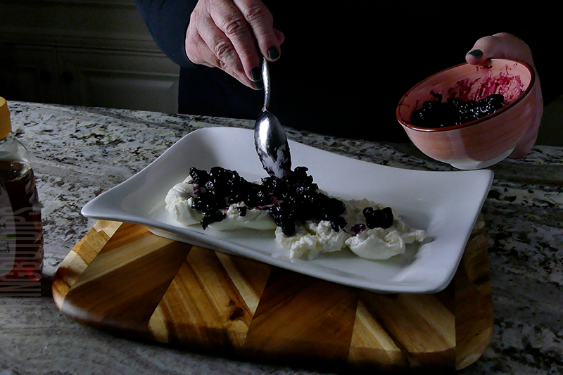 spooning blueberry compote on top of the creamy burrata cheese to create a simple appetizer