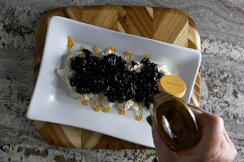 drizzling honey on the blueberry compote and burrata cheese