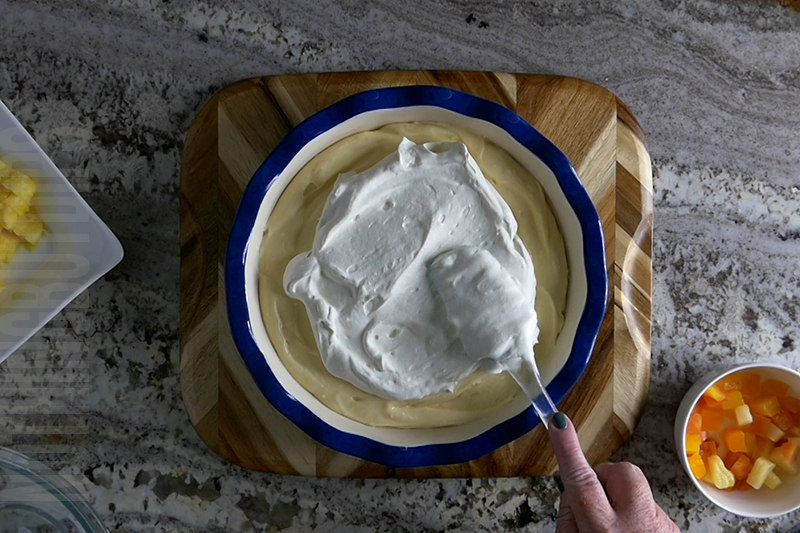 topping the tropical fruit dip dessert with fresh whipped cream