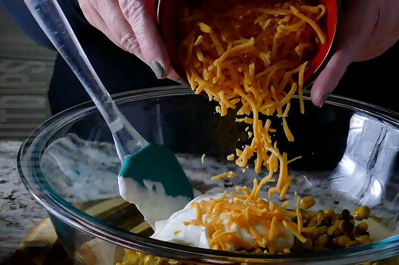 adding cheddar cheese to the bowl when making Mexican street corn dip