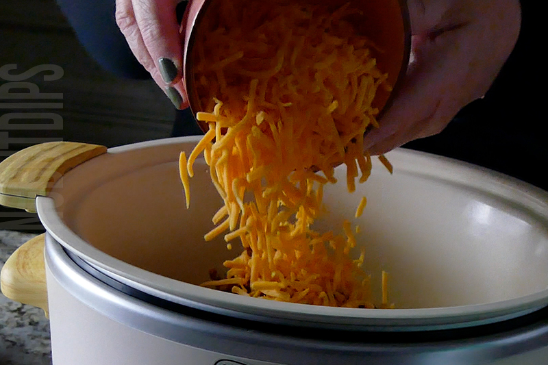 adding shredded cheddar to the crockpot for cheesy corn and bacon
