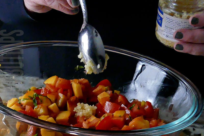 adding minced garlic to the peach and tomato bruschetta