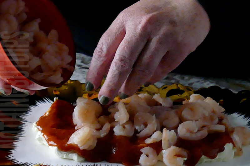 adding mini cocktail shrimp to cream cheese and cocktail sauce to create a dip