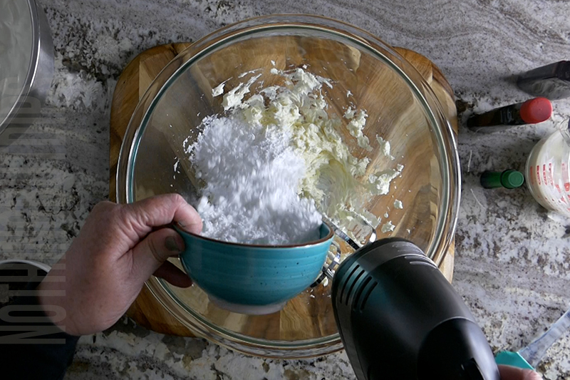 adding powdered sugar to the bowl to make mint chocolate chip dip