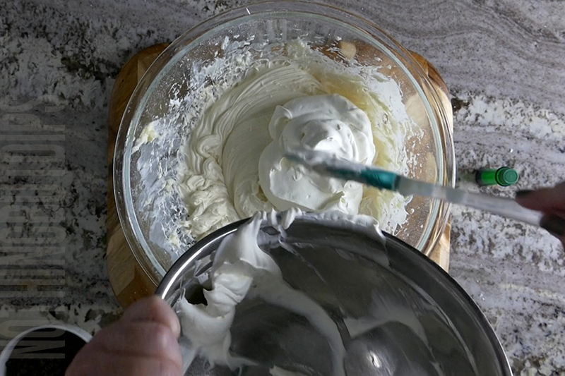 folding in whipped cream to the bowl to make mint chocolate chip dip