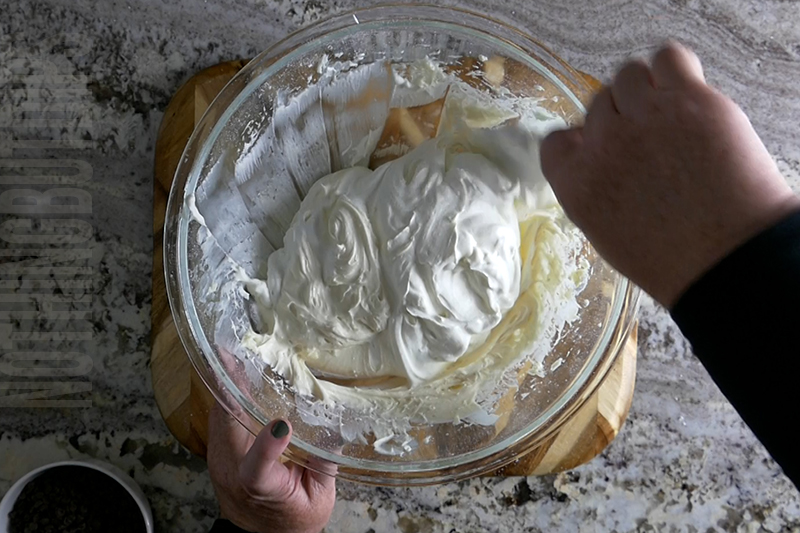 folding in whipped cream to the bowl to make mint chocolate chip dip