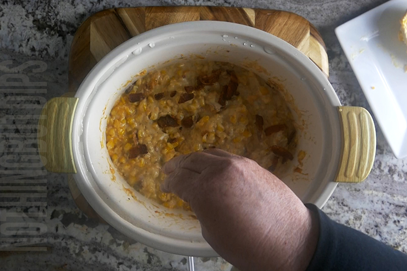 garnishing the crockpot cheesy corn and bacon dip with more bacon crumbles