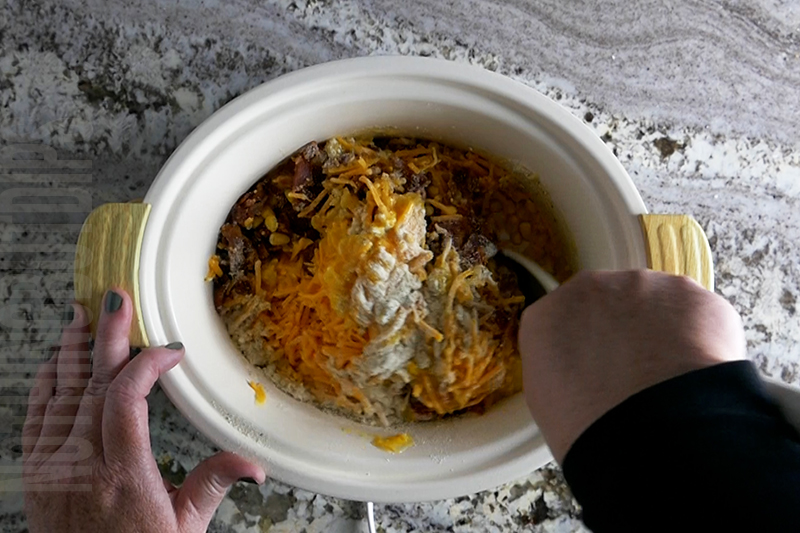 mixing together the ingredients in the crockpot to make cheesy corn and bacon dip